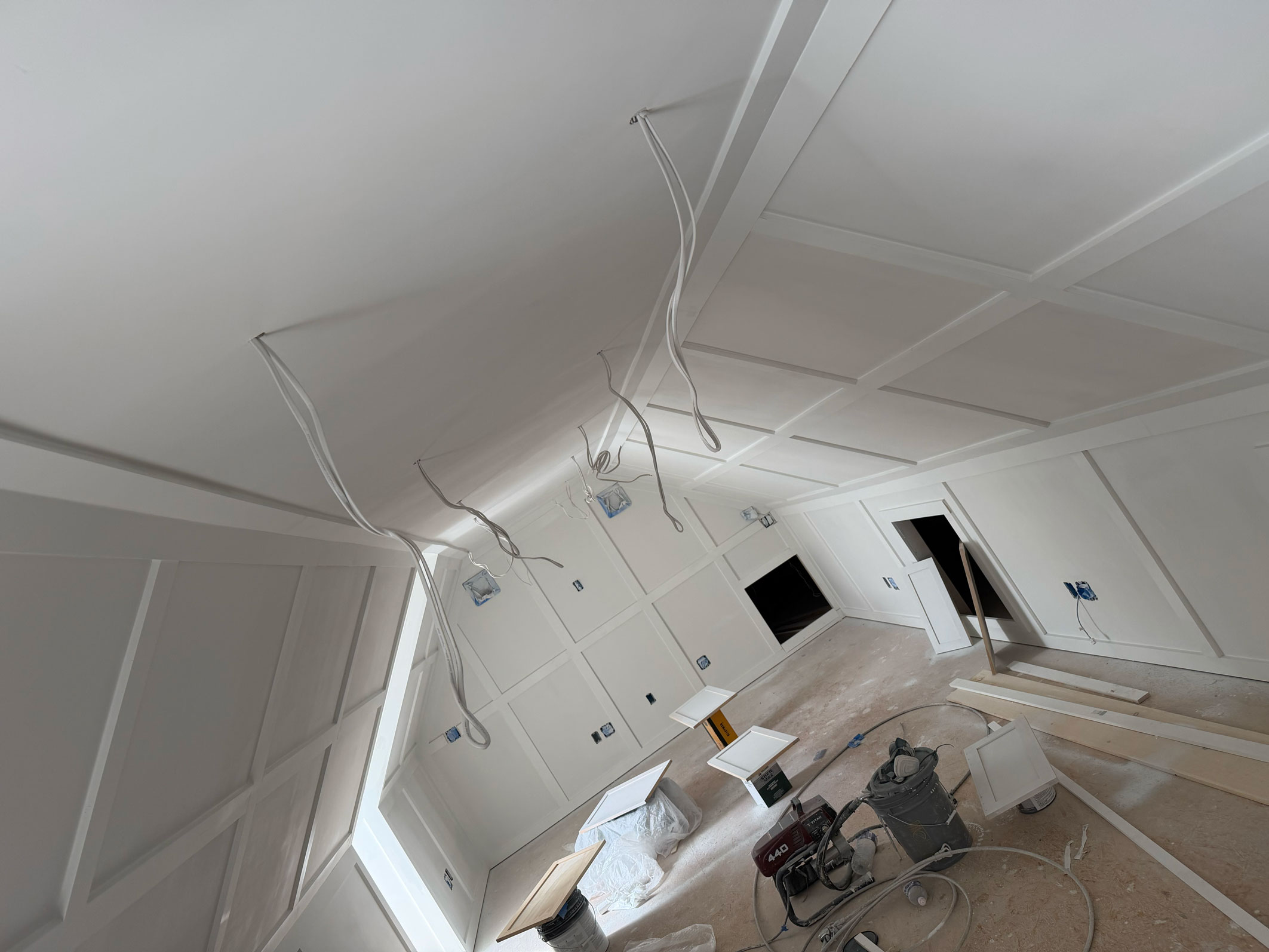 A room under construction with exposed wiring, unfinished walls, tools, and wood planks on the floor.