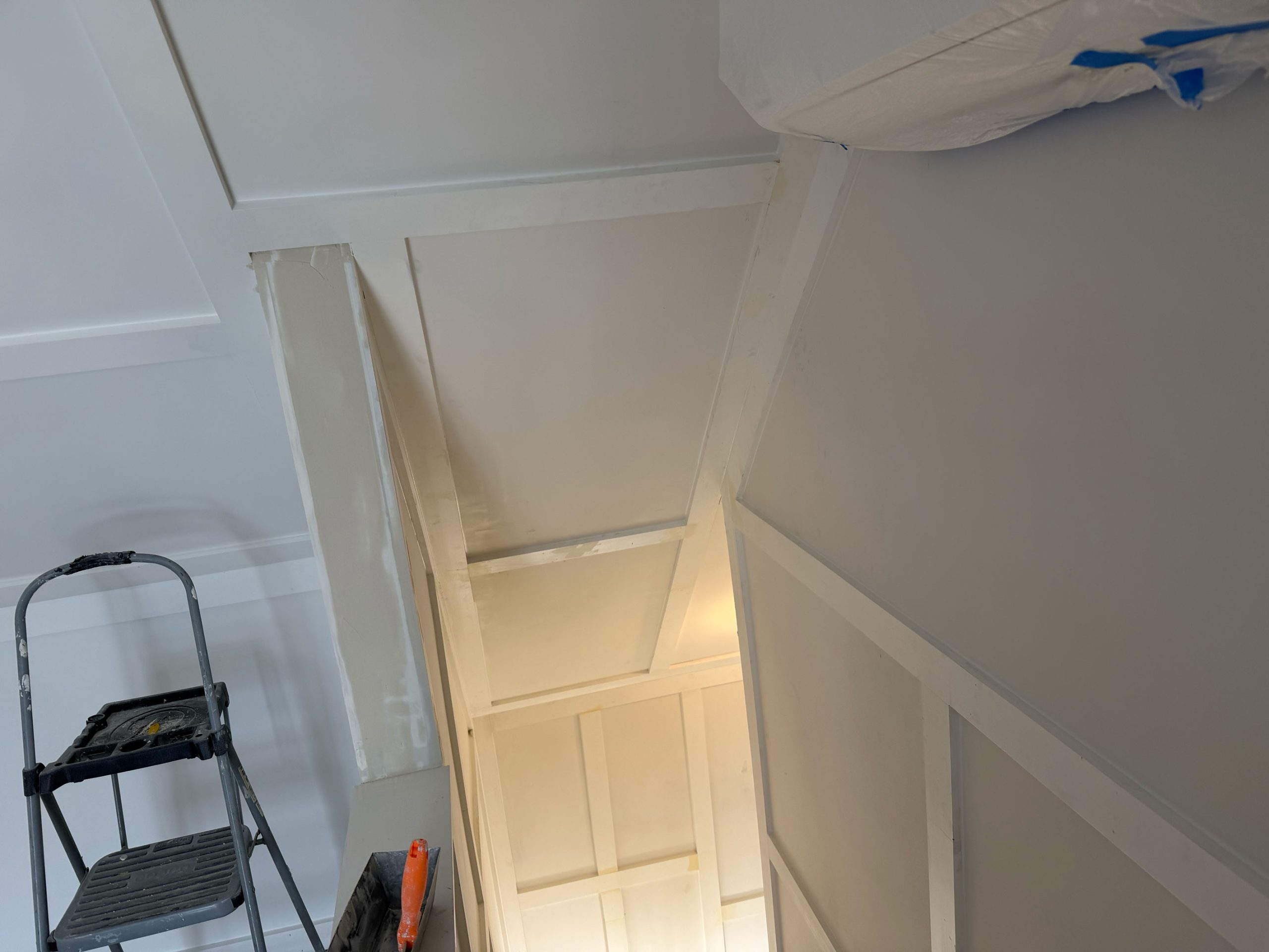 View of a stairwell under renovation with white walls, a step ladder, and painting supplies visible.