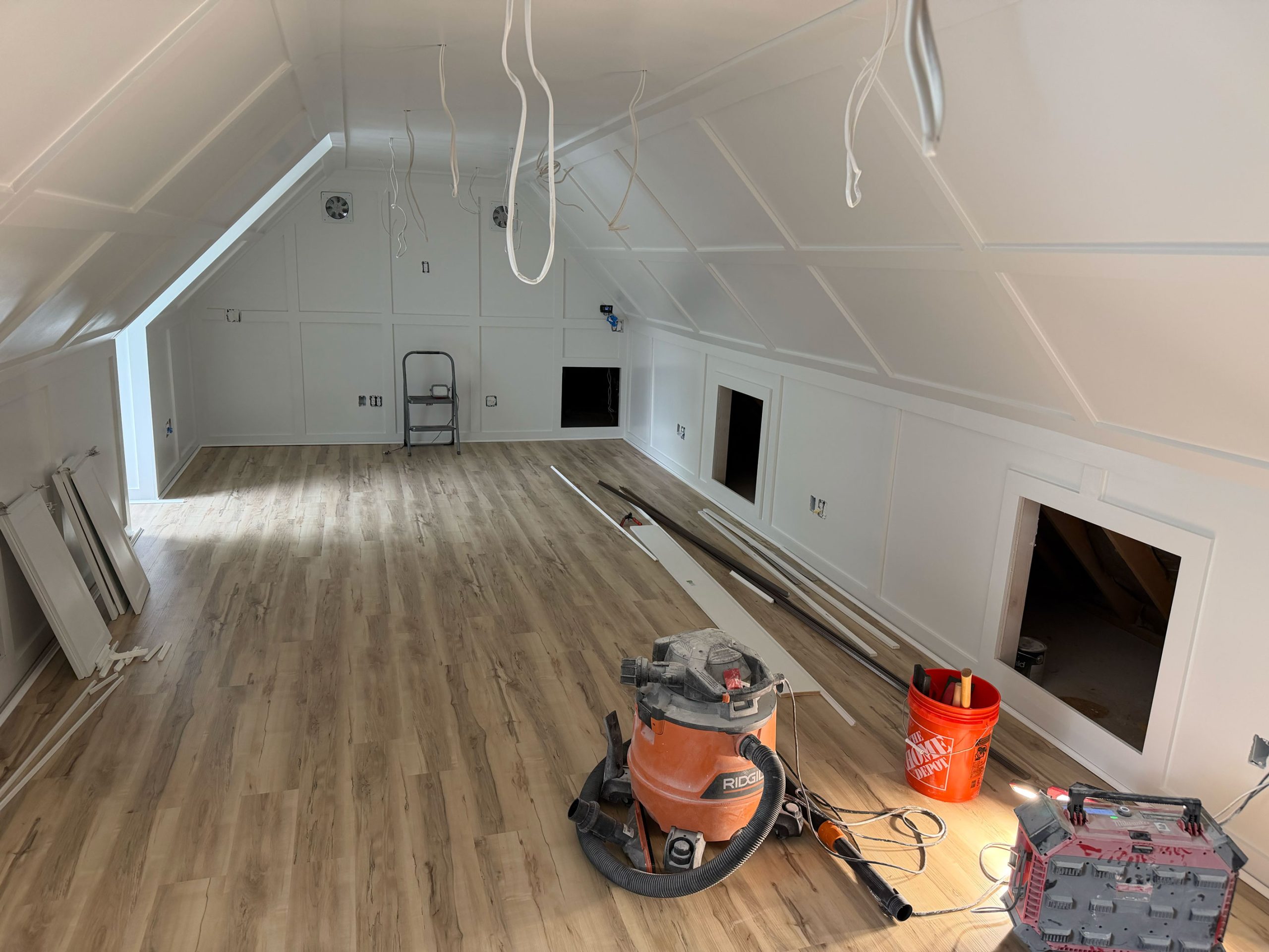 Unfinished attic room with wood flooring, tools, and construction materials scattered around.