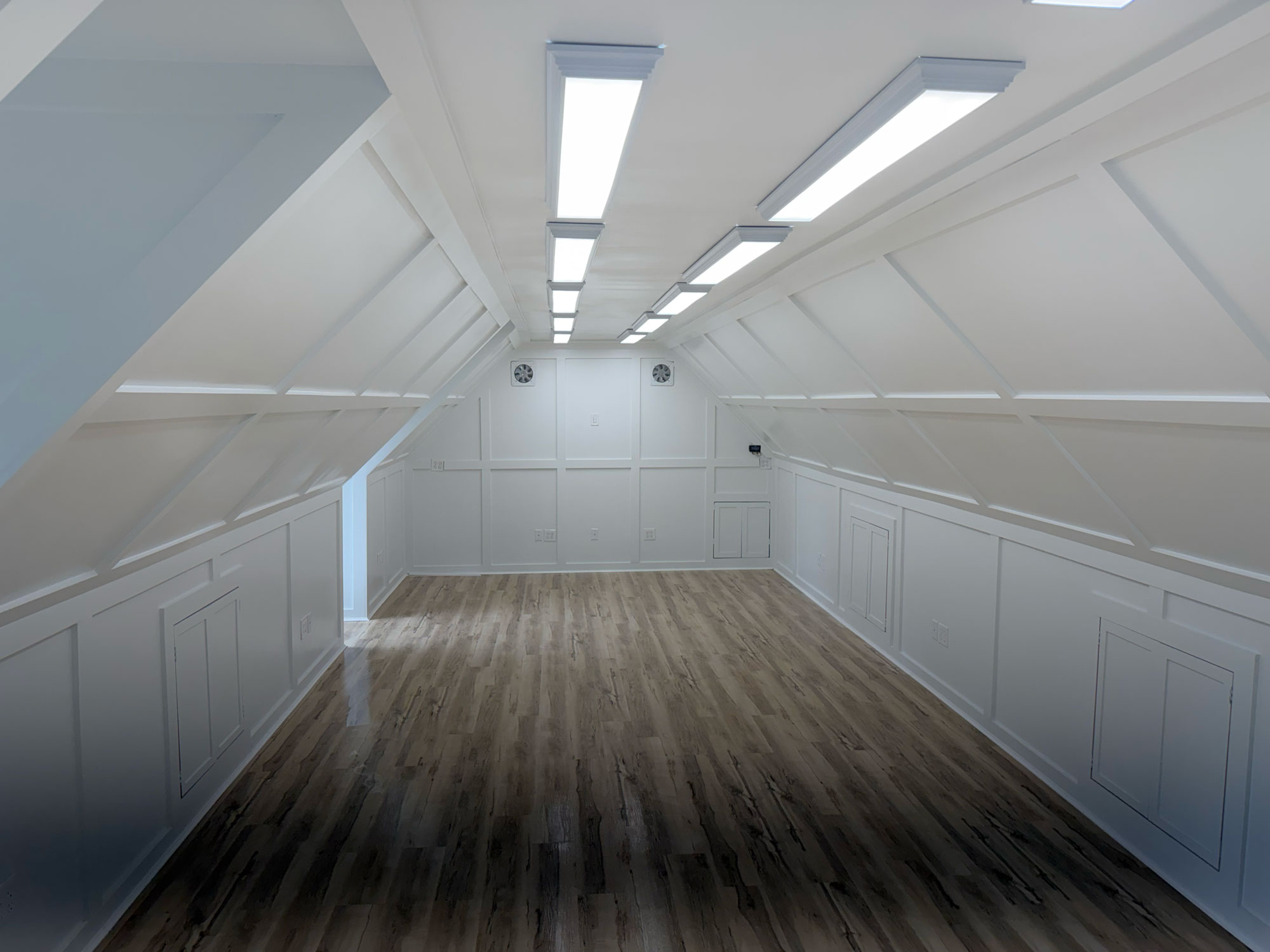 Bright, modern attic room with wood floors, white paneled walls, and ceiling lights.