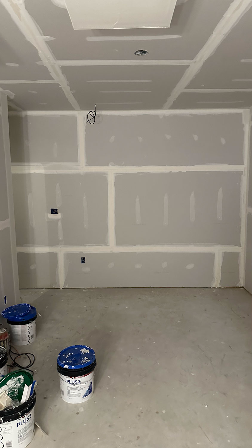 Room under construction with unfinished drywall, joint compound, and paint buckets on the bare floor.