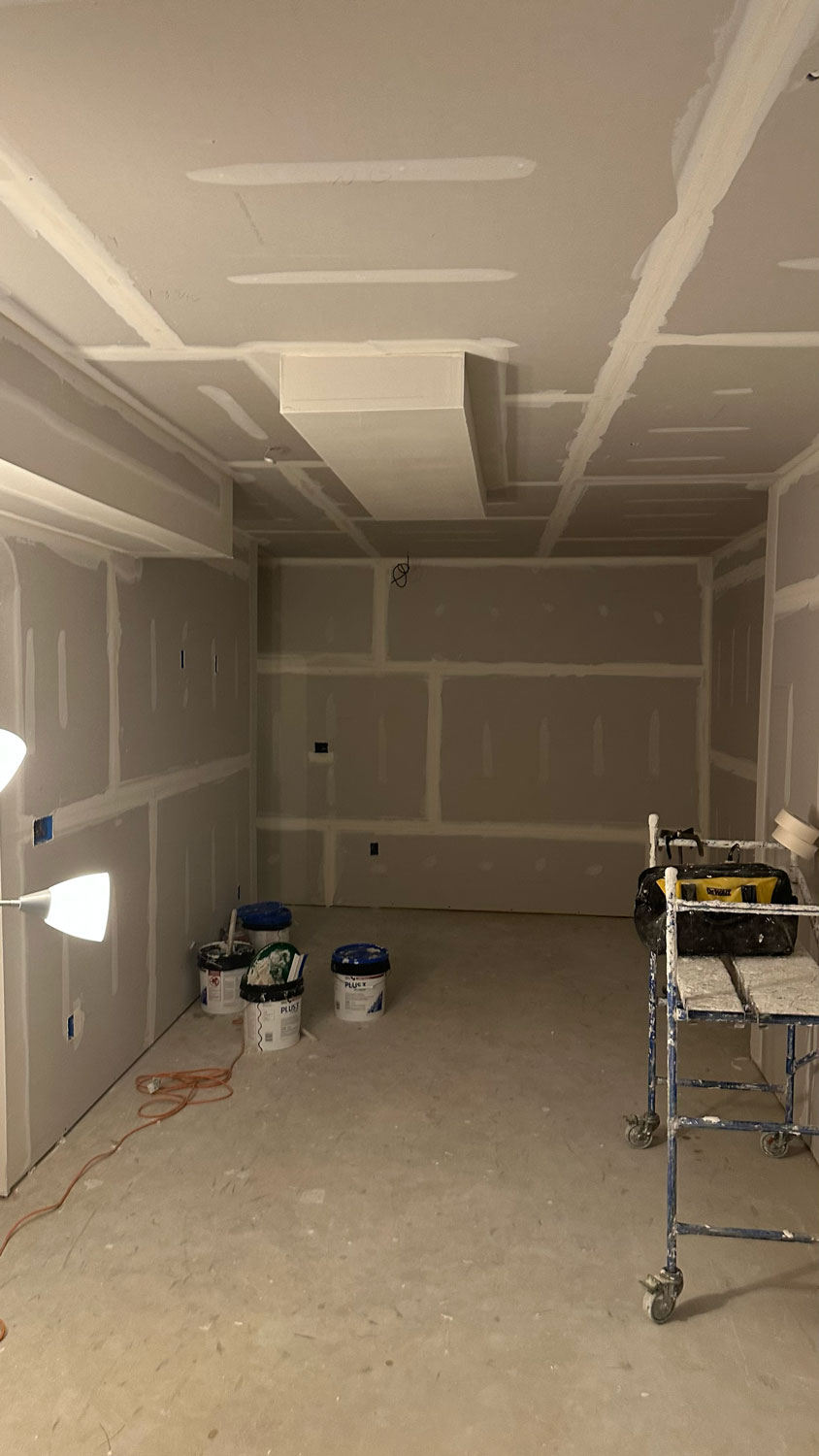 Room under construction with unfinished drywall, painting supplies, a scaffold, and a floor lamp.