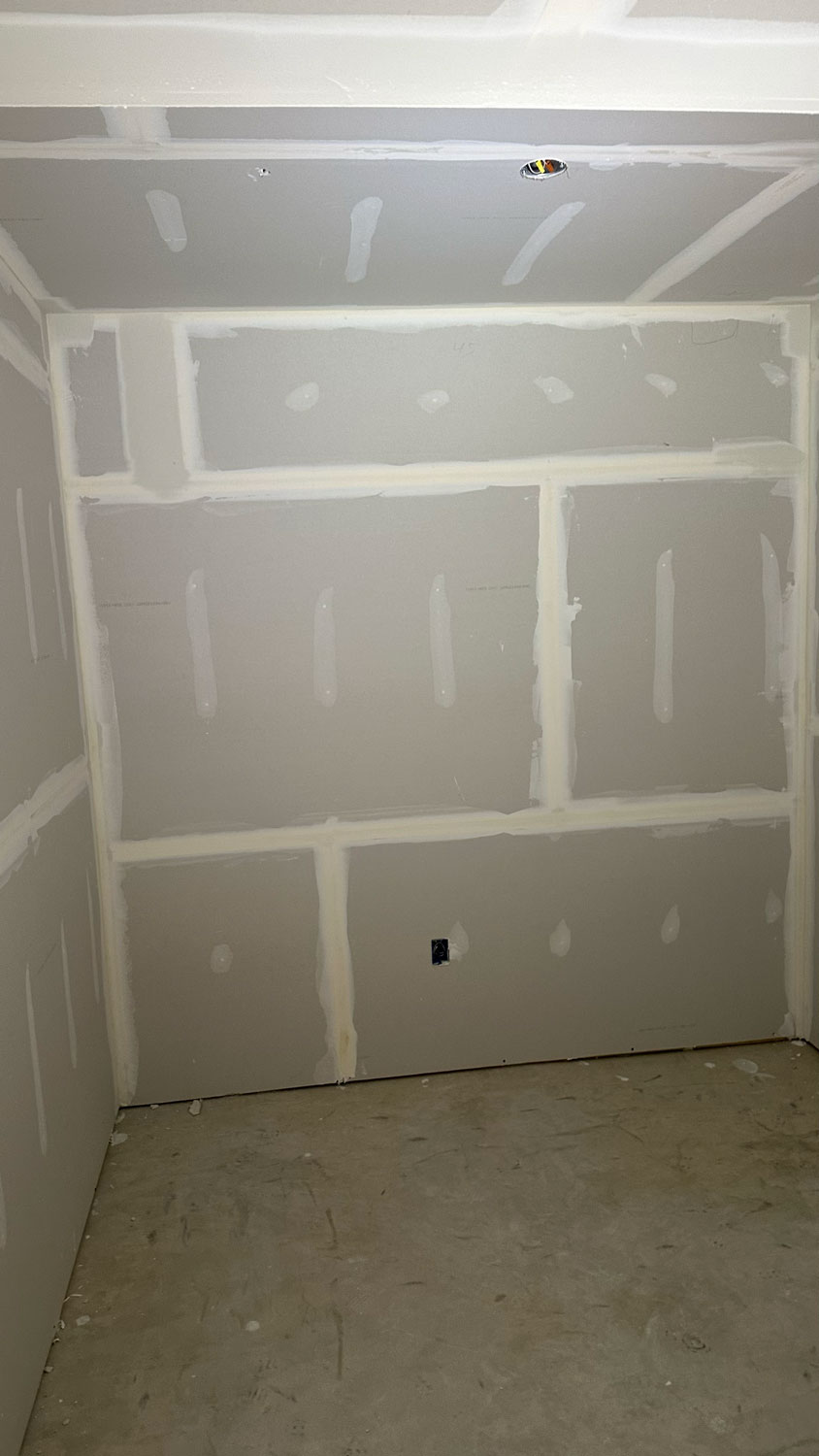 A small room with unfinished drywall, taped seams, and a bare concrete floor.
